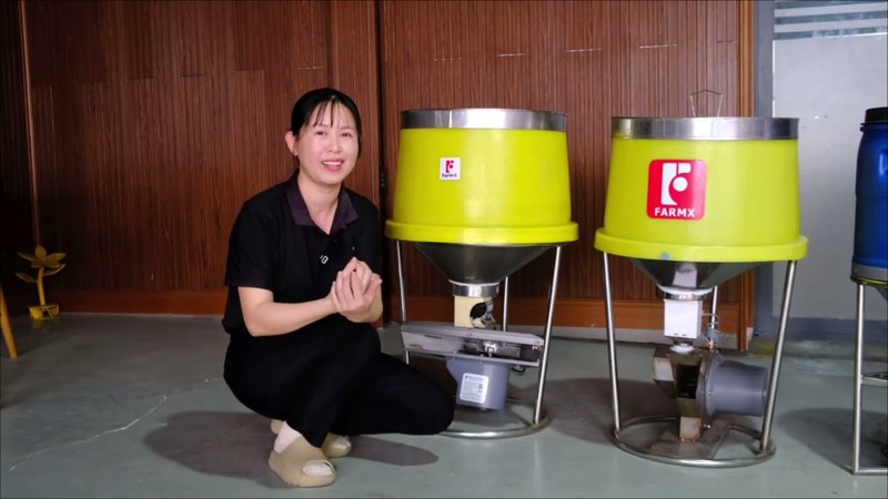 Ảnh bìa clip khám phá các loại máy cho tôm ăn FarmX, nhân viên xưởng ngồi cạnh hai máy phễu vàng trong nhà xưởng